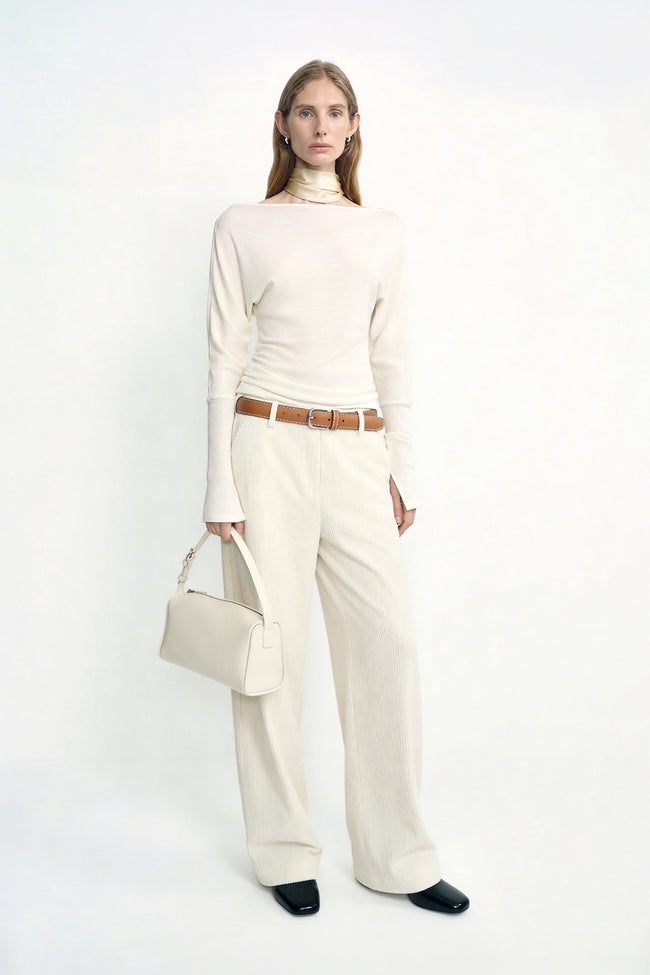 A model wearing Rue Sophie’s Talia Wide Leg Corduroy Pant in Winter White, styled with an ivory long-sleeve top, a light satin scarf around the neck, a cream handbag, and dark square-toe shoes.