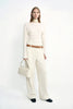 A model wearing Rue Sophie’s Talia Wide Leg Corduroy Pant in Winter White, styled with an ivory long-sleeve top, a light satin scarf around the neck, a cream handbag, and dark square-toe shoes.